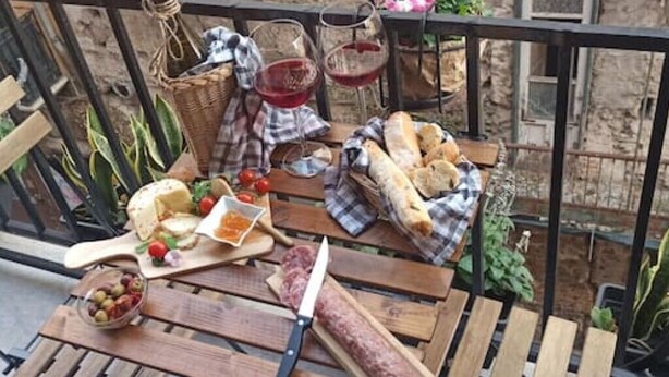 A wooden table with a variety of food items including cheese, bread, and olives, set on a balcony with a stone wall background. - Jacona 365 Apartment - In the historic center area of Palermo. (Palermo)