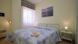 Un dormitorio con cama, mesita de noche, cortinas en la ventana y un cuadro en la pared.