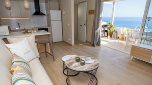 Een moderne woonkamer met een bank, een ronde salontafel en uitzicht op zee.