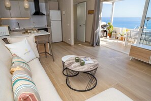 Uma sala de estar moderna com sofá, mesa de centro redonda e vista para o mar.