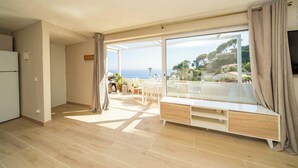 Ein modernes Wohnzimmer mit einem großen Schiebeglasfenster, das auf einen Balkon mit Meerblick führt.