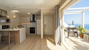 Eine moderne Küche mit Einbau-Mikrowelle, Backofen und Spüle, ein Essbereich mit Barhocker und ein Balkon mit Grill und Topfpflanzen.