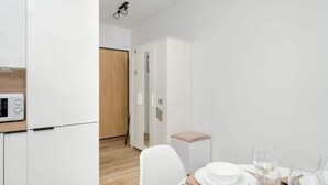 Una cocina compacta con gabinetes blancos, un microondas y un comedor con una mesa lista para dos.