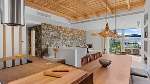 Cozinha moderna com parede de pedra, teto de madeira e área de jantar com uma mesa grande e cadeiras.