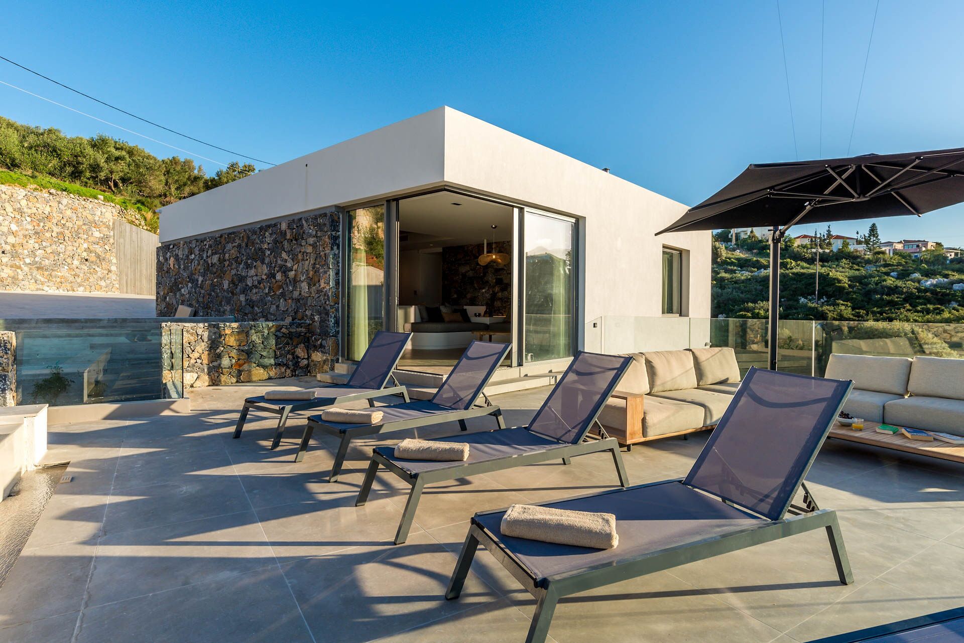 A modern outdoor lounge area with sun loungers and a glass-enclosed patio.