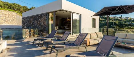 A modern outdoor lounge area with sun loungers and a glass-enclosed patio.