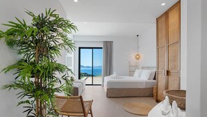 Quarto de hotel moderno com cama, uma cadeira, uma planta e vista para o mar.