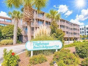 A sign for the Tilghman Beach & Racquet Club with a multi-story building in the background.