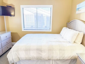 A bedroom with a bed, a dresser, a television, and a window with blinds.