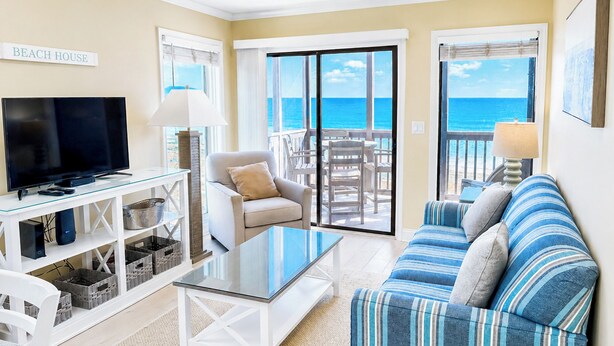 A living room with a TV, sofa, and a balcony with a view of the ocean. - Experience Tilghman Beach and Racquet Club Unit 308! Oceanfront, Pools, Tennis, Close to Main Street! (North Myrtle Beach)