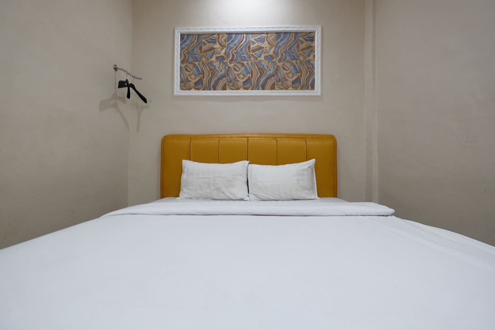 Una cama bien hecha con un cabecero amarillo, ropa de cama blanca y una obra de arte abstracta enmarcada encima.