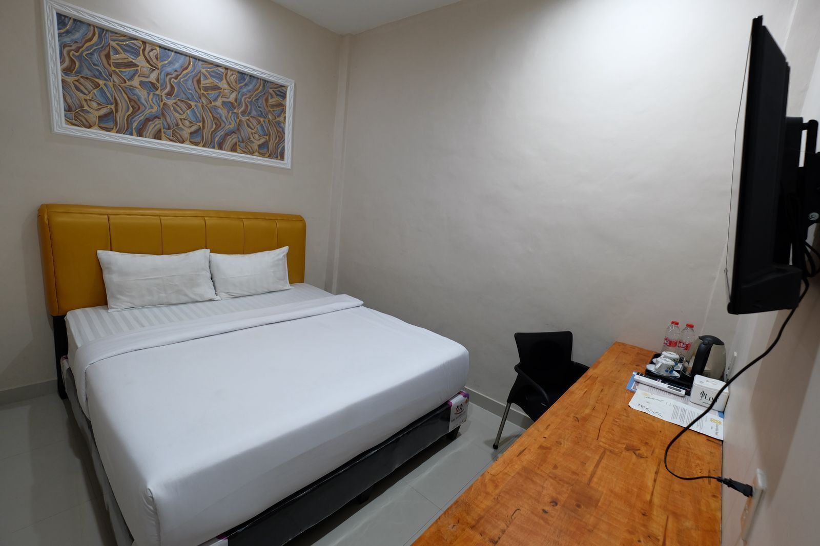 Una habitación de hotel con una cama, un escritorio de madera, una silla, un televisor y una obra de arte en la pared.