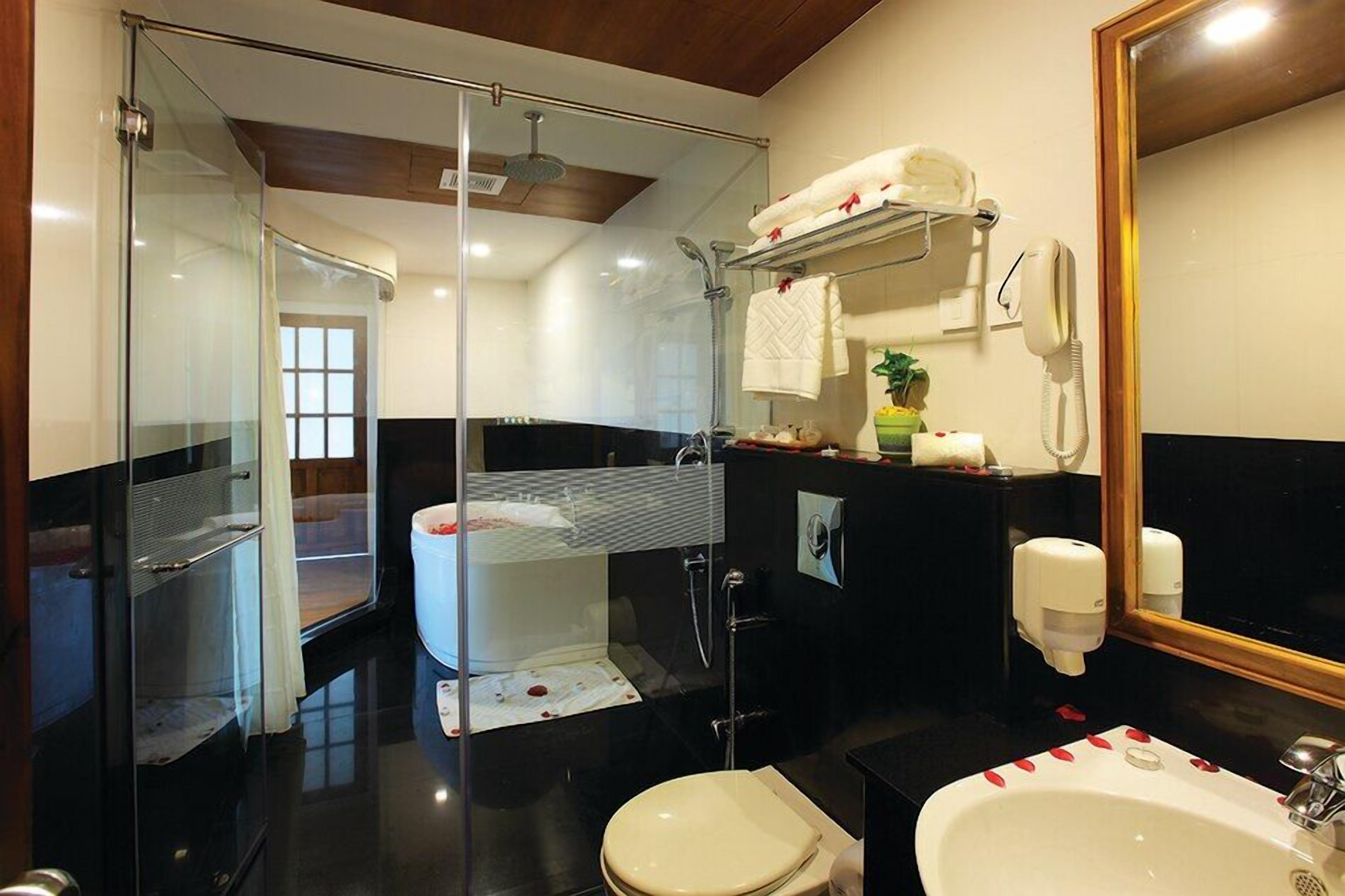 Un baño moderno con cabina de ducha de vidrio, inodoro blanco, lavabo con espejo y toallero con toallas.