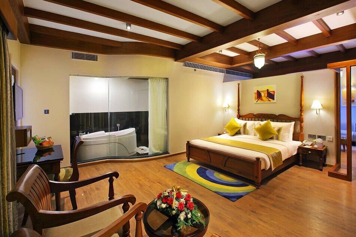 A spacious hotel room with a large bed, a sitting area with a chair and a table, a small desk, and a bathroom with a bathtub.