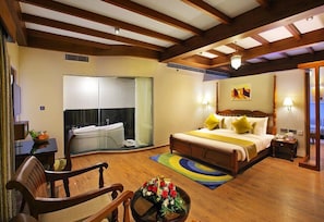 A spacious hotel room with a large bed, a sitting area with a chair and a table, a small desk, and a bathroom with a bathtub.