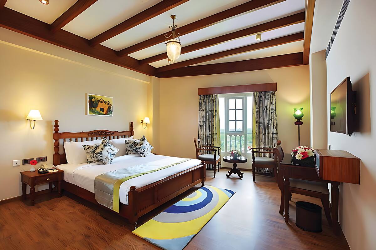 A hotel room with a wooden bed, bedside lamps, a desk with a chair, a TV, and a window with curtains.