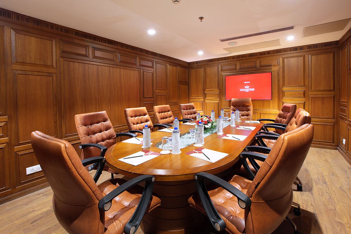 A conference room with a wooden panel wall, a large screen, and leather chairs around a wooden table.