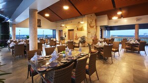 A spacious outdoor dining area with wicker chairs and tables set for guests, featuring a view of the ocean and a wooden ceiling. - LE MARITIME KOCHI (Kochi)