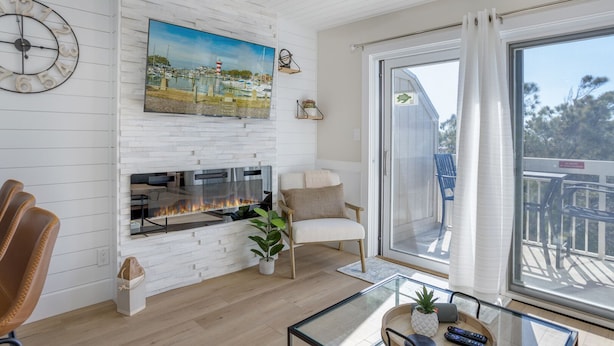 A living room with a fireplace, a large painting of a marina, a comfortable chair, and a glass coffee table. - Amazing 1-bd Beach Villa, best location Hilton Head Island -Heart of the Island! (Hilton Head Island)