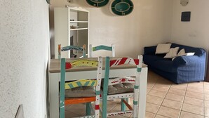 Uma sala de estar com área de jantar, um sofá azul e um armário branco com prateleiras.