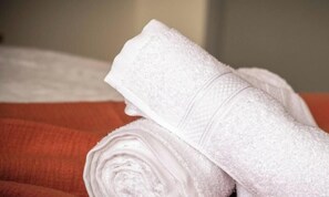 Une serviette blanche, soigneusement pliĂ©e, est posĂ©e sur un lit recouvert dâune couverture rouge.