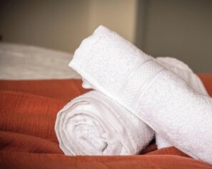Ein ordentlich gerolltes weißes Handtuch auf einem Bett mit einer roten Decke.