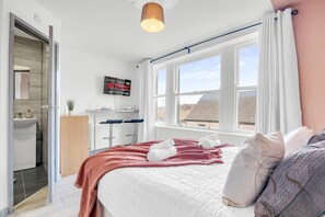 Ein modernes Schlafzimmer mit Bett, Fernseher, Fenster und Badezimmer.