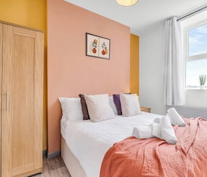 A bedroom with a bed, pillows, a blanket, a wardrobe, a window with curtains, and a plant on the windowsill. - Studio 1E – Cozy Stay with Wi-Fi + TV (Stoke-on-Trent)