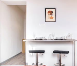 A minimalist kitchen with a white countertop, two bar stools, and a framed artwork above. - Studio 1E – Cozy Stay with Wi-Fi + TV (Stoke-on-Trent)