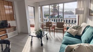 A living room with a sofa, chairs, a coffee table, a TV, and a balcony with a railing. - Apartamento Amplio y Tranquilo con Vistas al Mar 4 (CN)