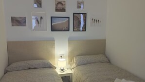A hotel room with two beds, a nightstand with a lamp, and a wall with framed pictures. - Apartamento Amplio y Tranquilo con Vistas al Mar 4 (CN)