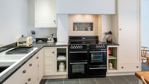 Une cuisine moderne avec des meubles blancs, une cuisinière noire et un four encastré.