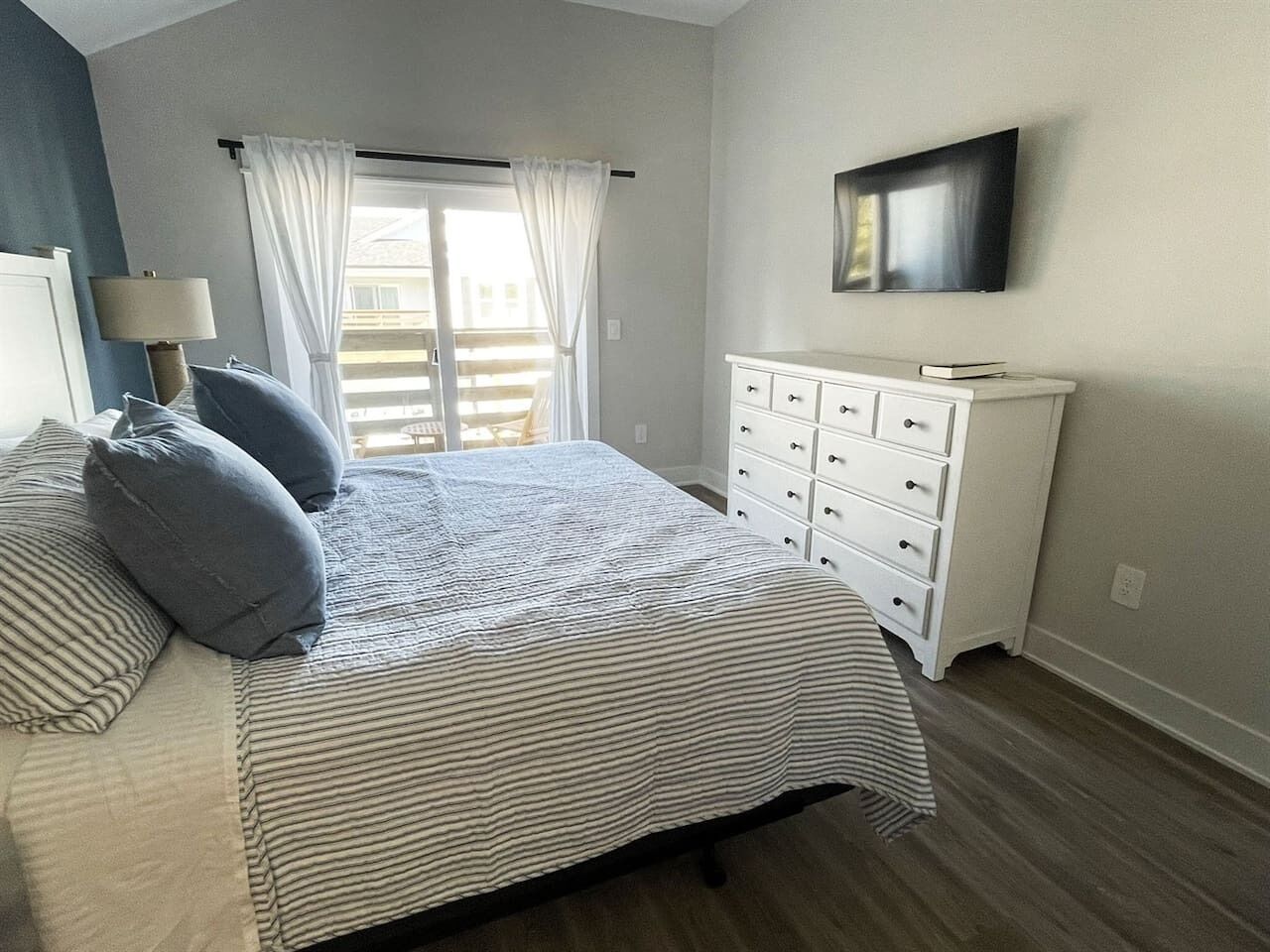 Un dormitorio con cama, cómoda, televisor y ventana con cortinas.