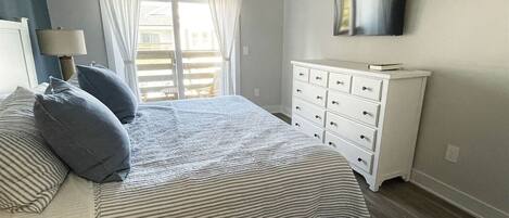 Un dormitorio con cama, cómoda, televisor y ventana con cortinas.