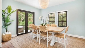 A dining area with a large table, white chairs, and a chandelier.