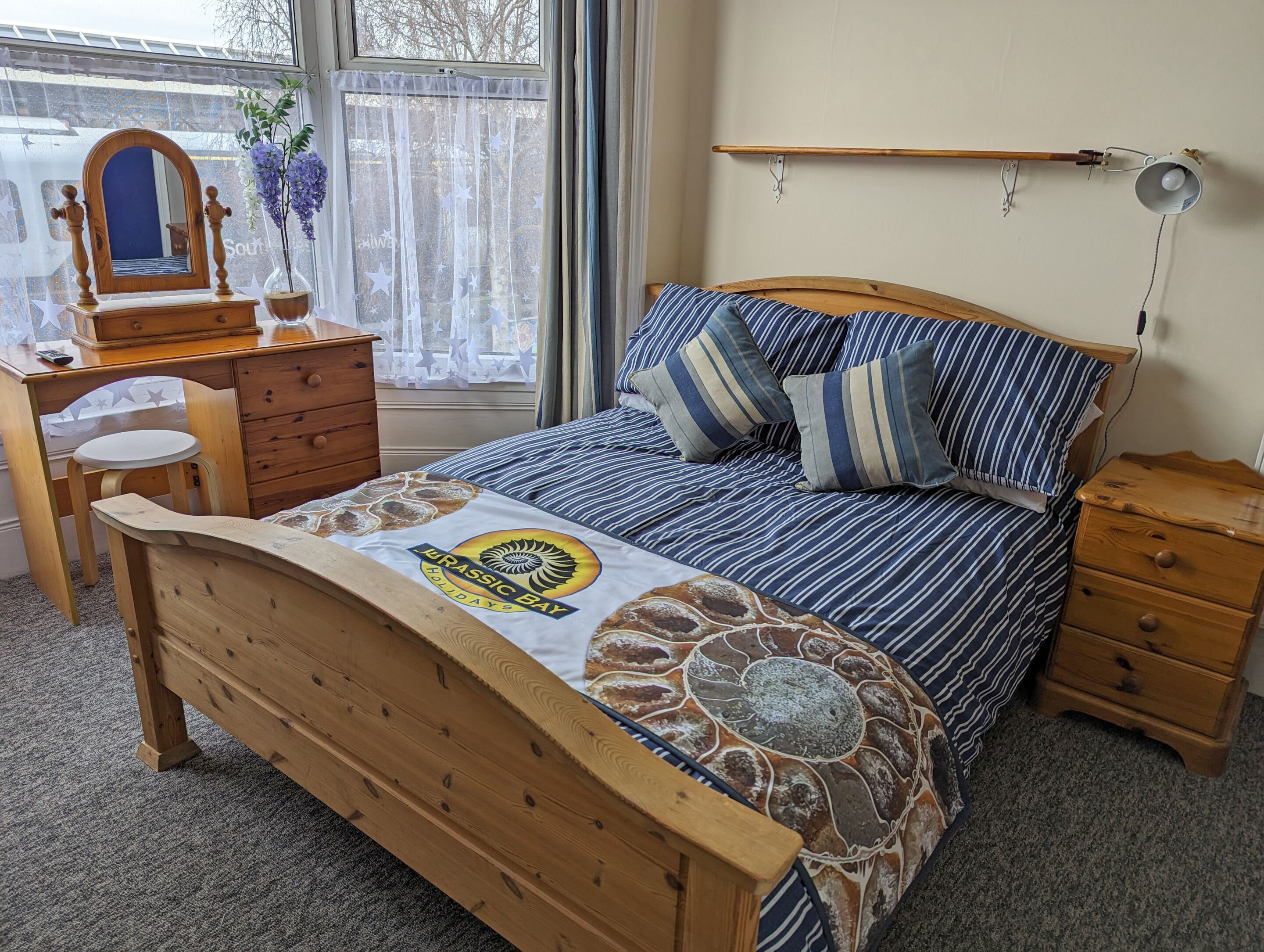 A bedroom with a wooden bed, striped bedding, a desk with a mirror, and a dresser.