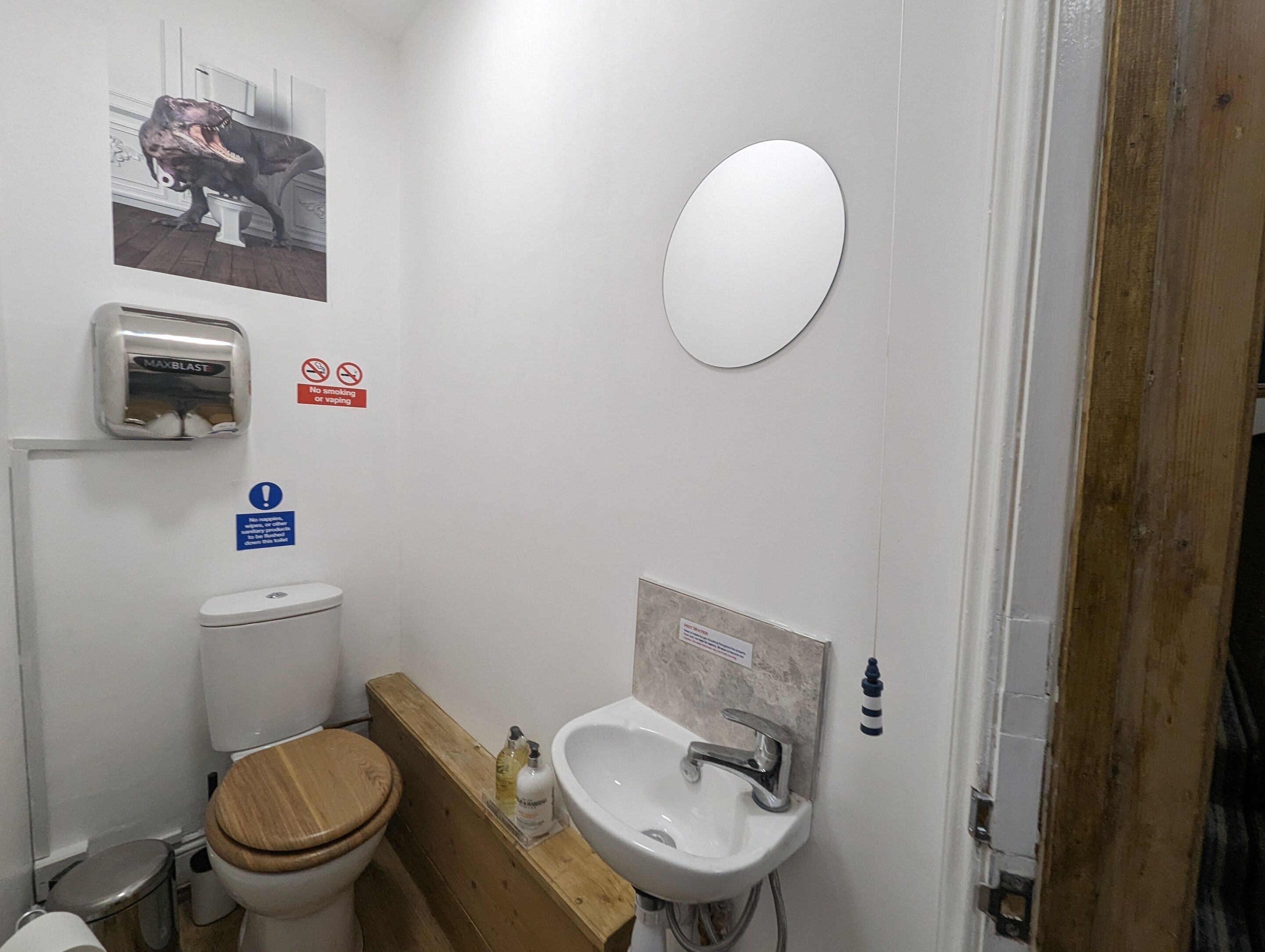 Un baño con inodoro, tocador de madera, lavamanos y secamanos.