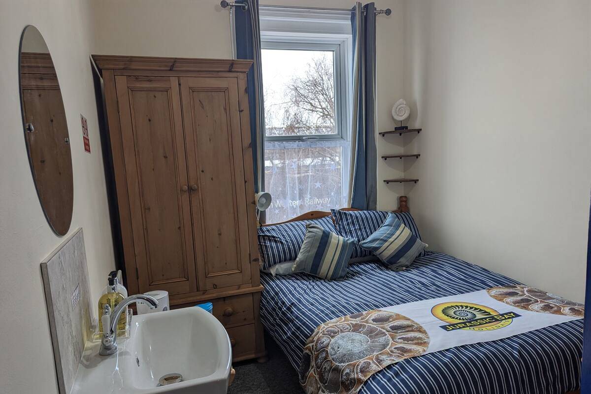 Un dormitorio con cama, un armario de madera, un lavabo blanco y una ventana con cortinas.
