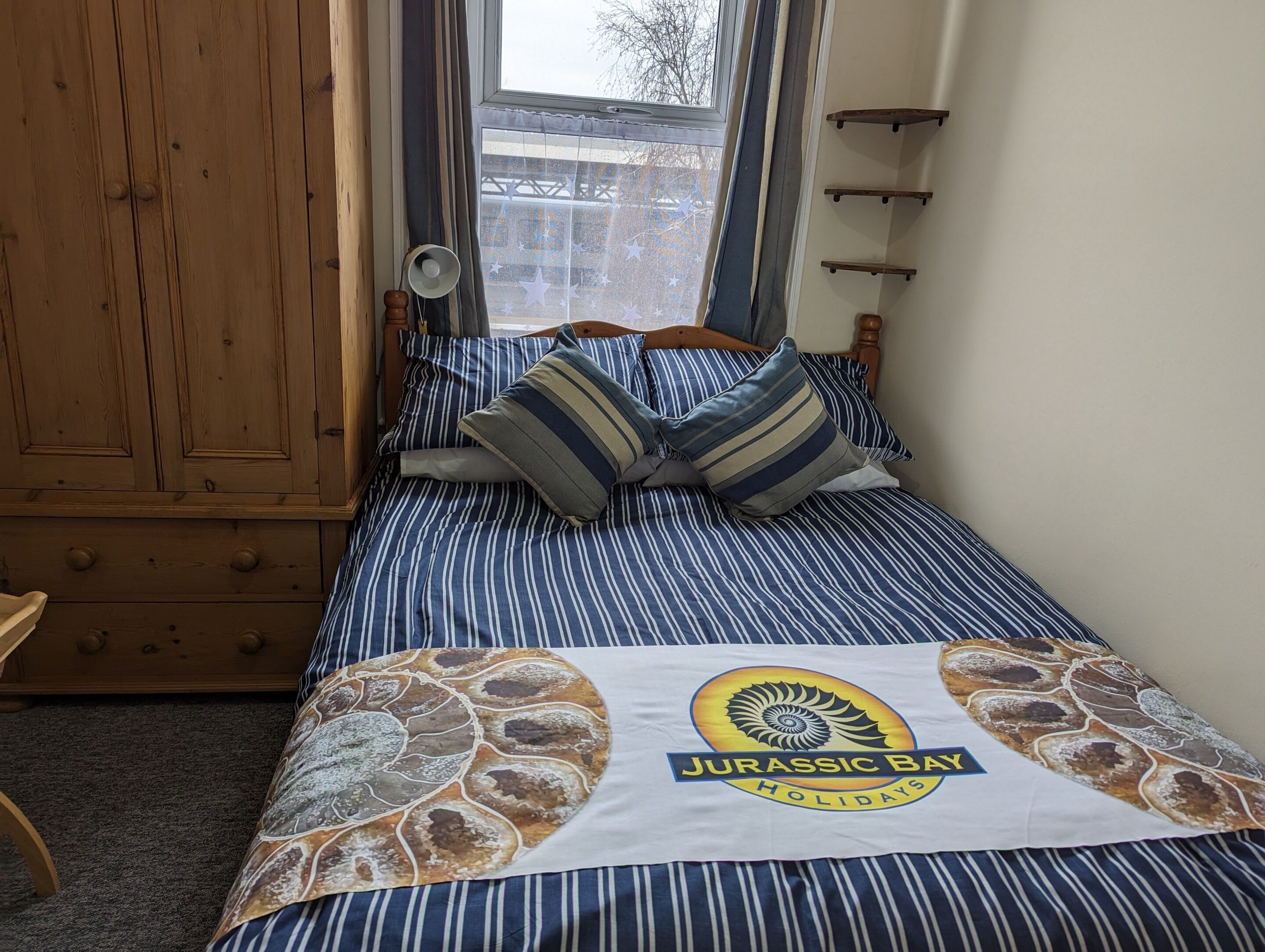 Un dormitorio con una cama, ropa de cama a rayas y una almohada con el diseño de 'Jurassic Bay Holidays'.