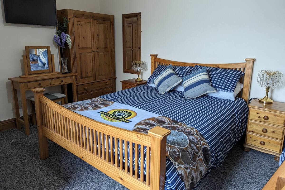 Un dormitorio con cama de madera, un escritorio, un armario y televisión en la pared.