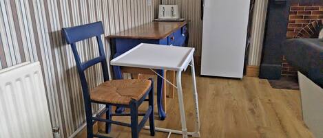 A compact kitchen with a striped wall, a wooden table, a white refrigerator, and a blue chair.