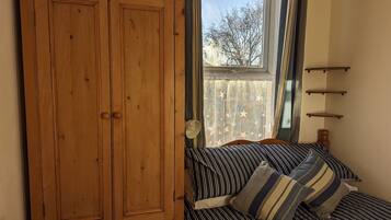 A bedroom with a wooden wardrobe, a bed with striped bedding, and a window with a view of trees.