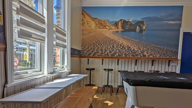 A room with a wooden floor, a pool table, a bench, and a mural of a beach. - Jurassic Bay Holidays (Weymouth)