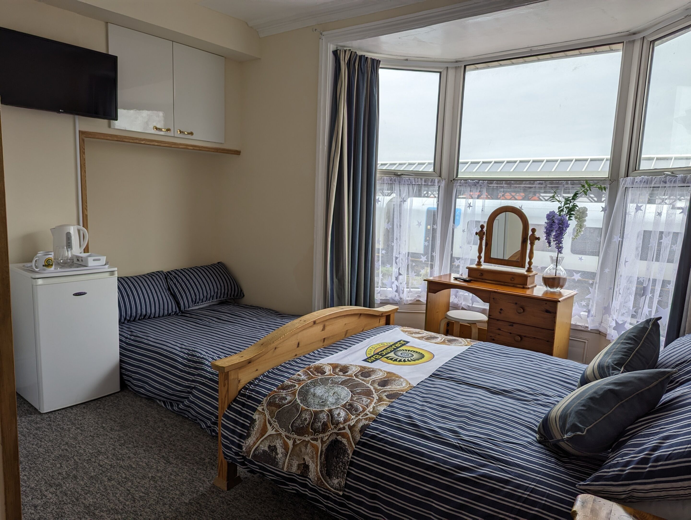 Een slaapkamer met een bed, een dressoir, een spiegel, een televisie en een raam met gordijnen.