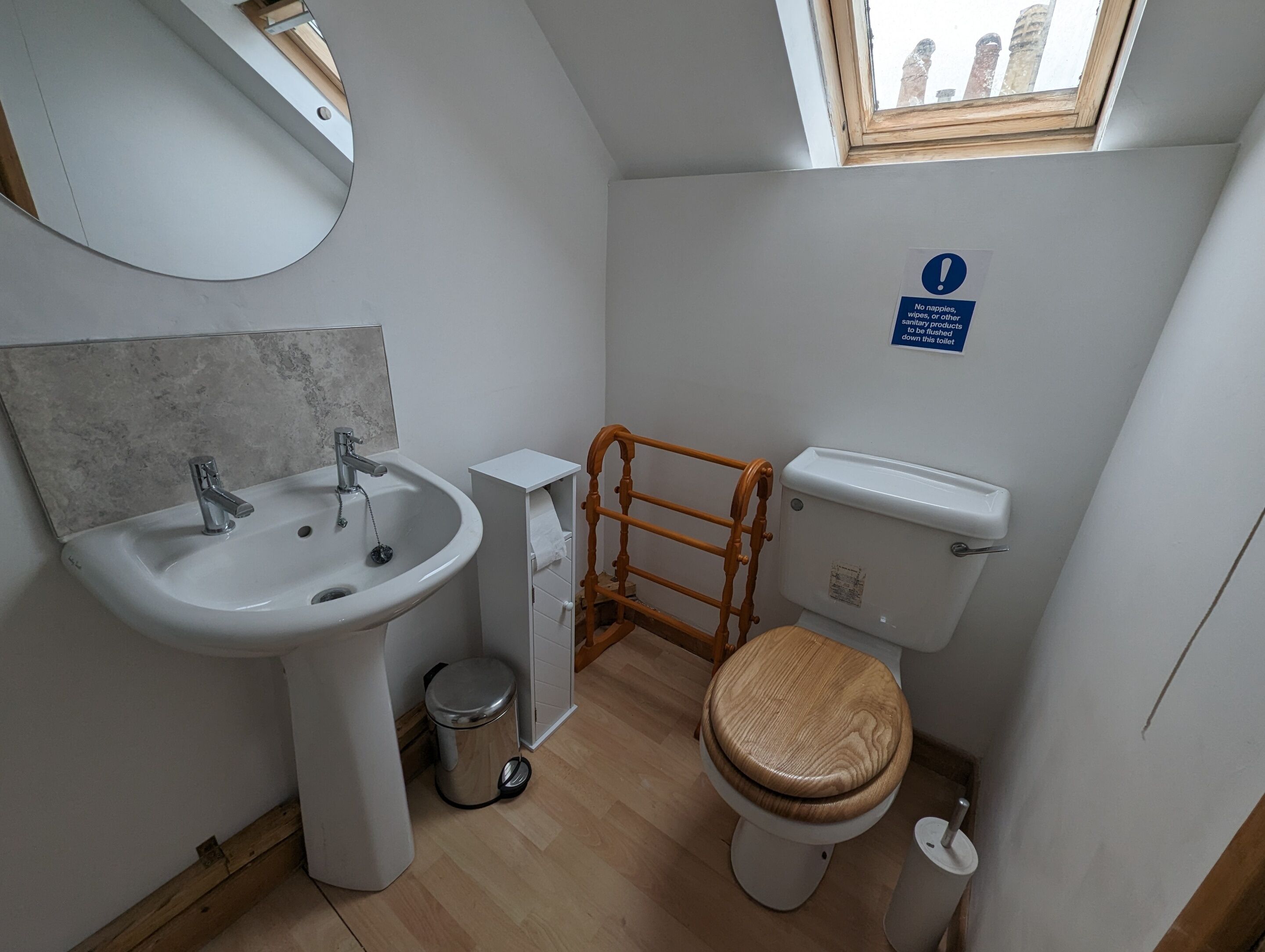 Ein kleines Badezimmer mit Waschbecken, Spiegel, Toilette und Fenster.