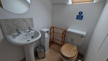 A compact bathroom with a sink, mirror, toilet, and a window.