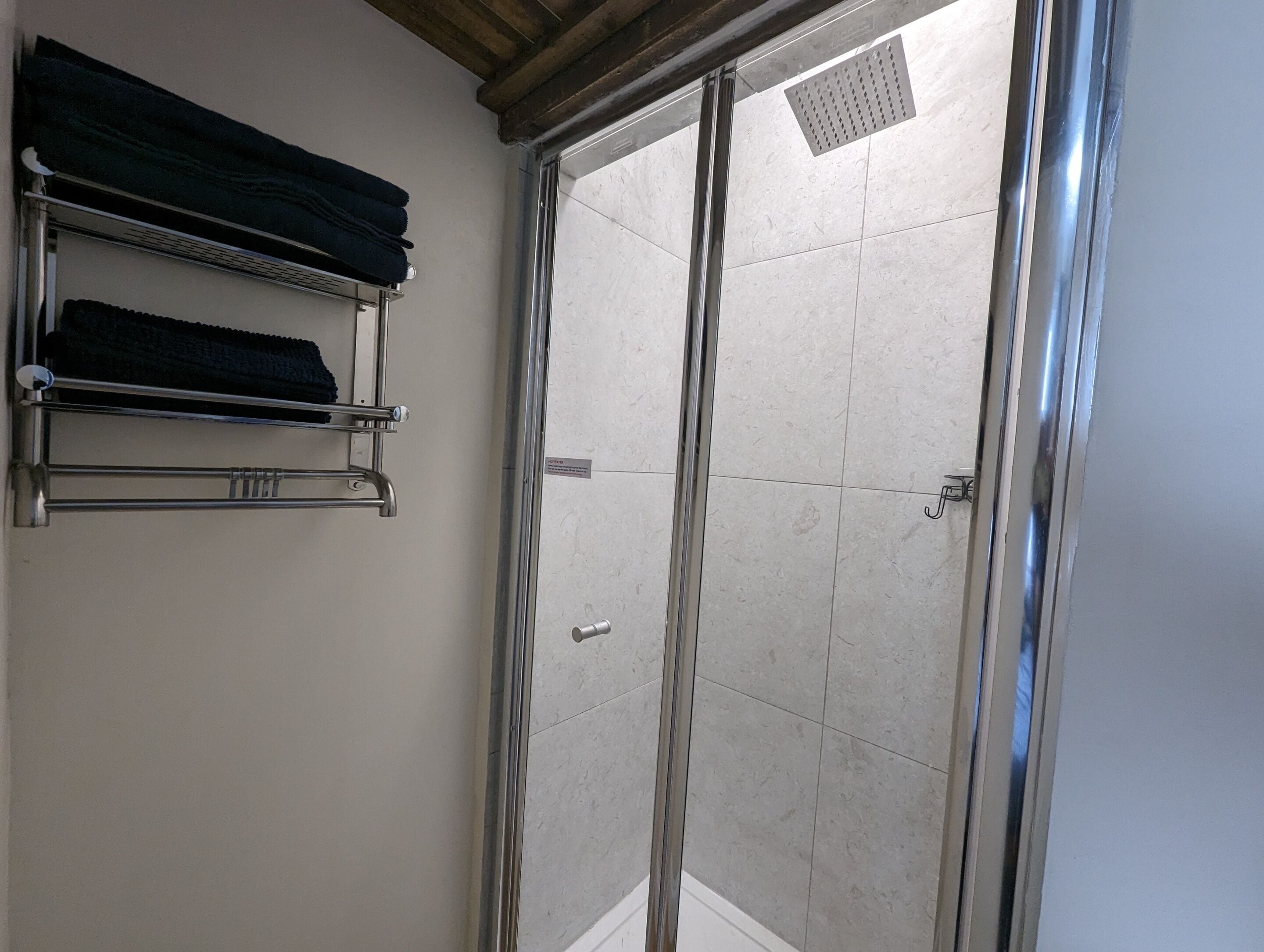 Un espace douche doté d’une porte en verre, d’un porte-serviettes avec des serviettes pliées et d’un sol carrelé.