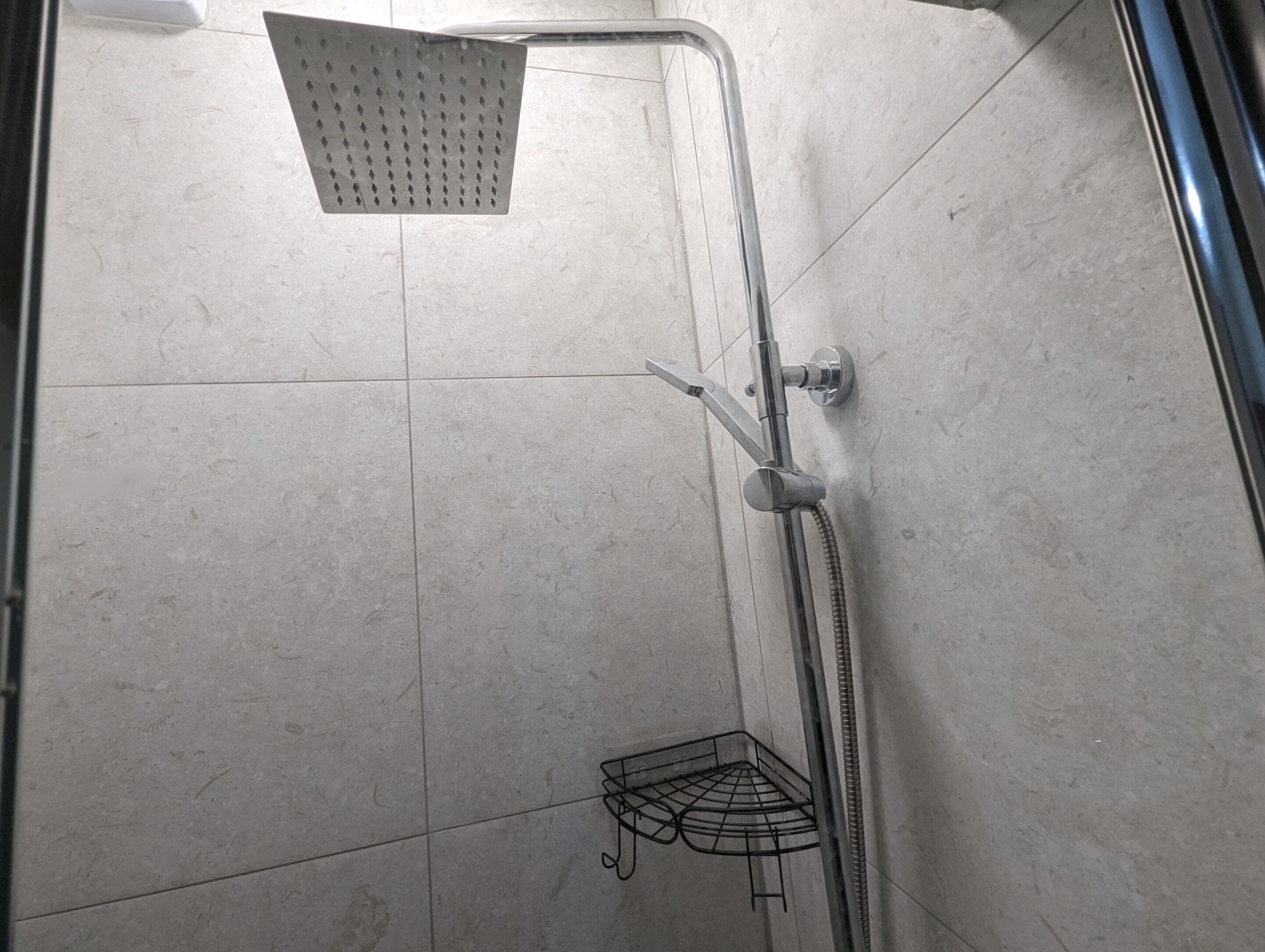 A corner of a bathroom with a shower, a towel rack, and a corner shelf.