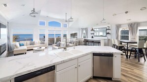 Una cocina moderna con una isla grande, armarios blancos y vista al océano.