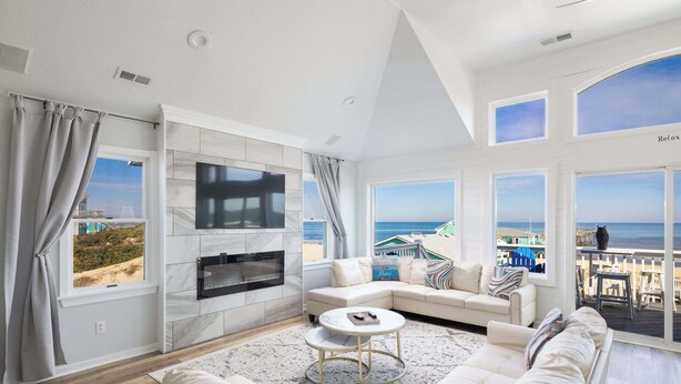 Un salón amplio con una televisión grande, asientos cómodos y vista a la playa.